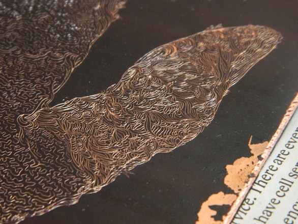 An intricately-patterned copper thumb sparkling through black wax
